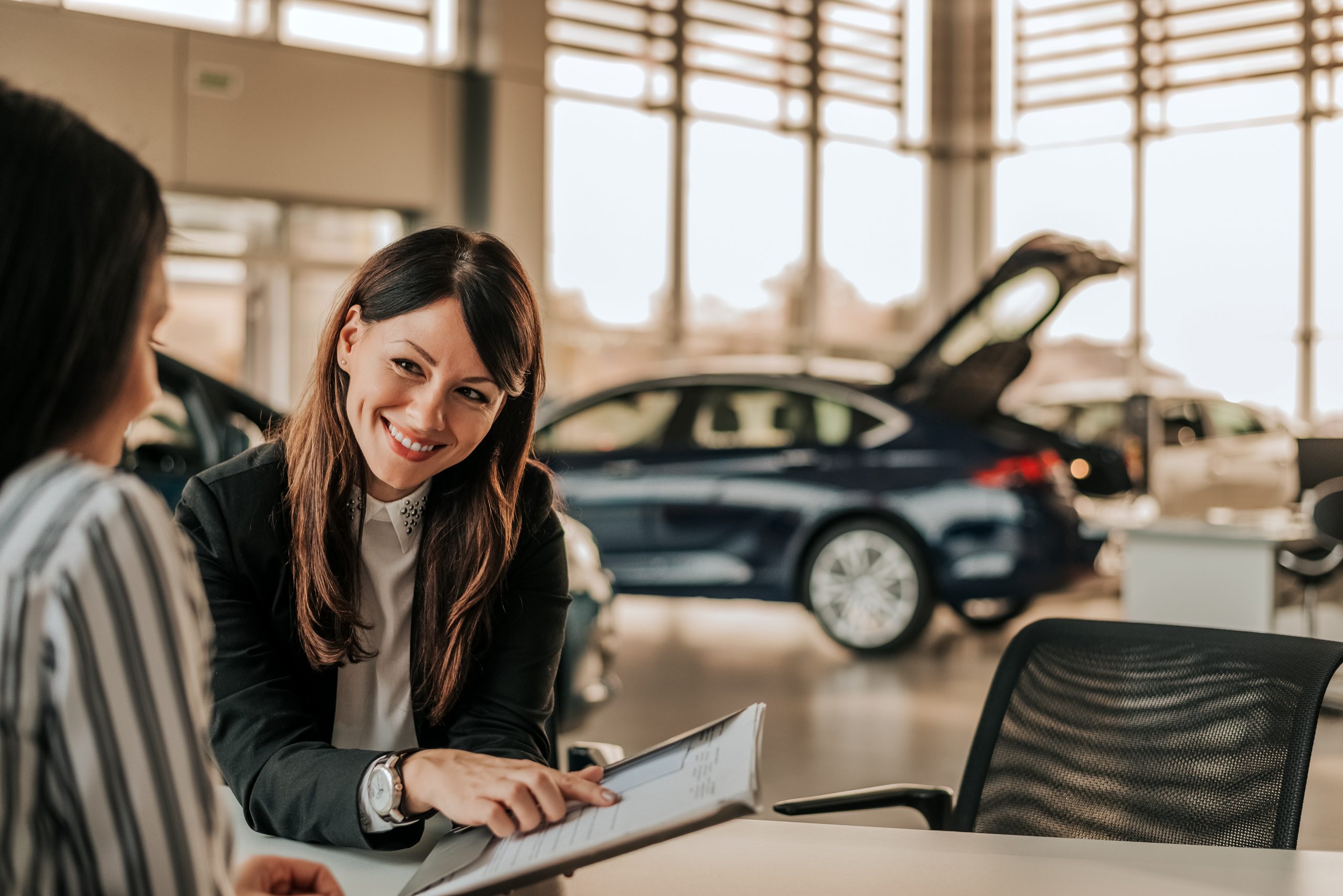 Smiling car saleswoman discussing  a contract with a female customer.